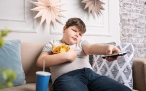 Obese child with snacks and controller on couch