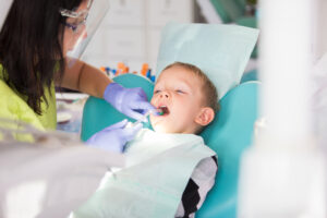 A young boy sitting in a dental chair smiling while a pediatric dentist gently examines his teeth.
