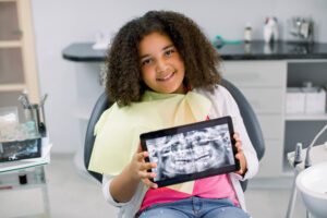 A smiling young girl holding up a digital X-ray of her teeth at Kids 360 Pediatric Dentistry.