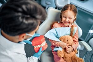 A Little Girl Sits In A Dental Chair Holds a Teddy Rabbit