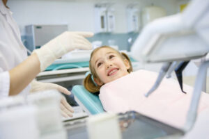 A relaxed and smiling young girl during a pediatric dental exam, demonstrating a positive, fear-free dentist visit.