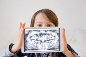 A preteen boy smiling and holding up a digital X-ray of his teeth on a tablet.