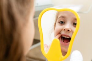 A young girl looking into a tooth-shaped yellow mirror and smiling at her teeth.