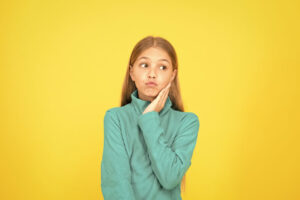 Young girl holding her cheek in pain against a yellow background.