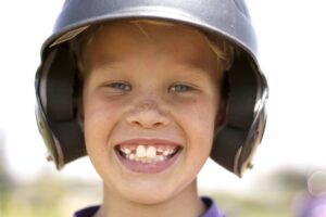 A young, smiling baseball player wearing a batting helmet at Kids 360 Pediatric Dentistry.