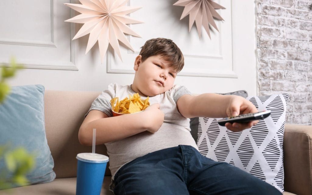 Obese child with snacks and controller on couch